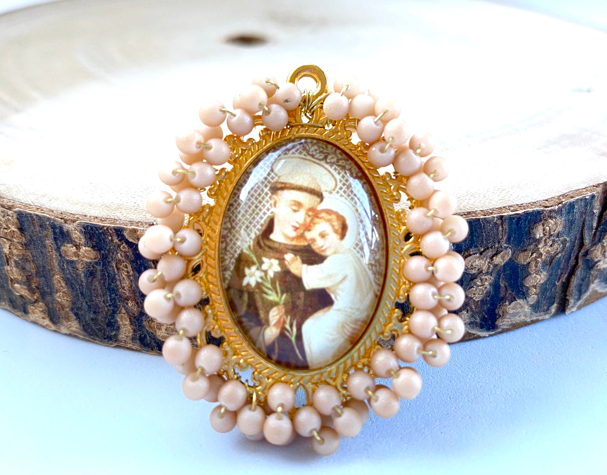 Medalla bordada con cuentas rosa palo e imagen de un santo con el Niño