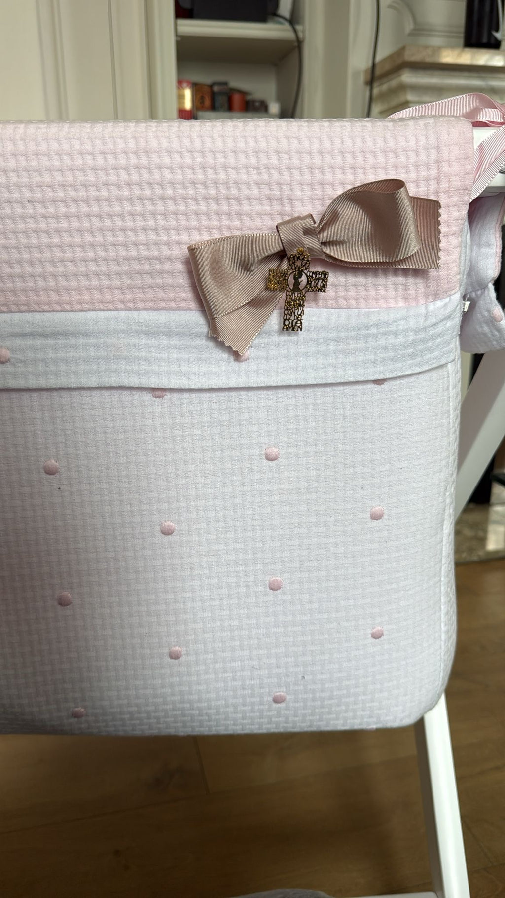 Lazo de cuna beige con cruz de oración colgado en una cuna de tela rosa