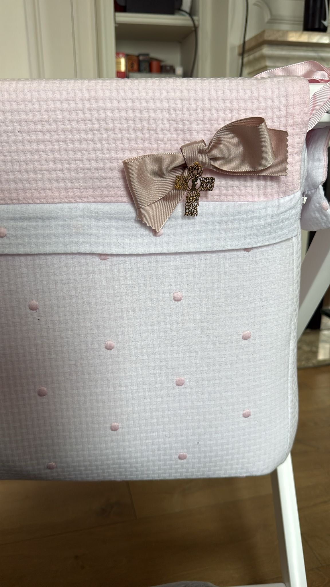 Lazo de cuna beige con cruz de oración colgado en una cuna de tela rosa