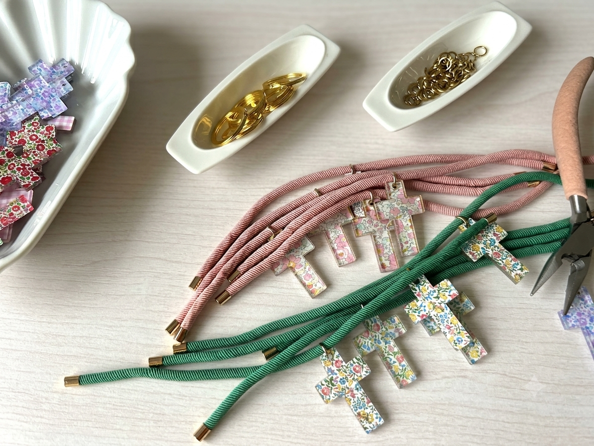 Mesa del taller con cruces de tela liberty, cordones rosas y verdes y anillas doradas para montar llaveros