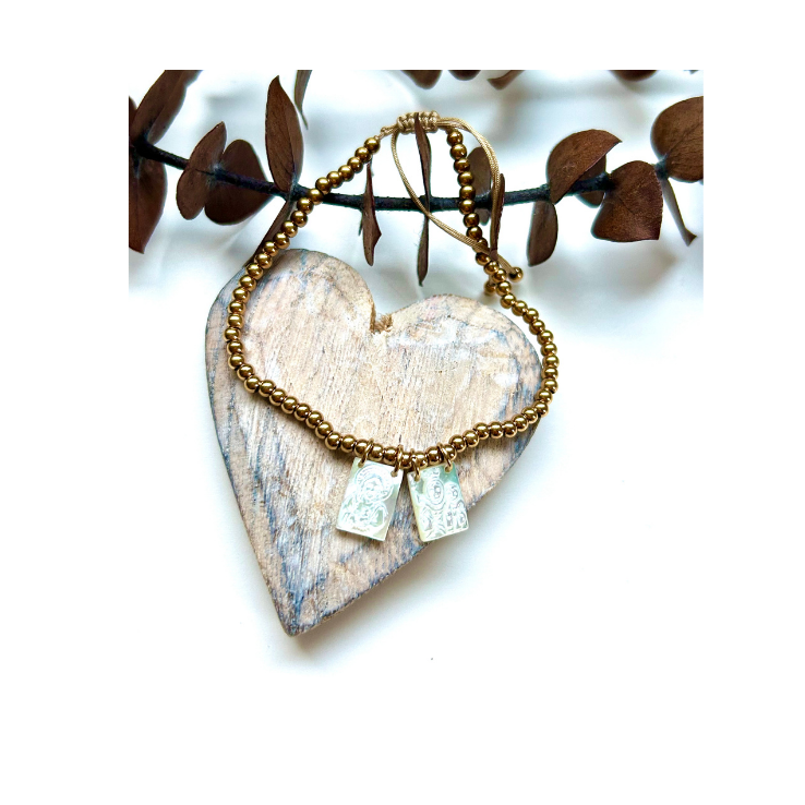 Pulsera escapulario de nácar con bolitas de acero doradas sobre un corazón de madera